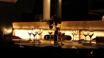 A dimly lit dining area with a table set for a meal, featuring a vase with dried flowers and several wine glasses.