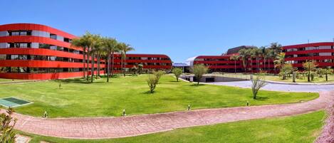 A modern building complex with curved red architecture, green lawns, and a paved walkway.