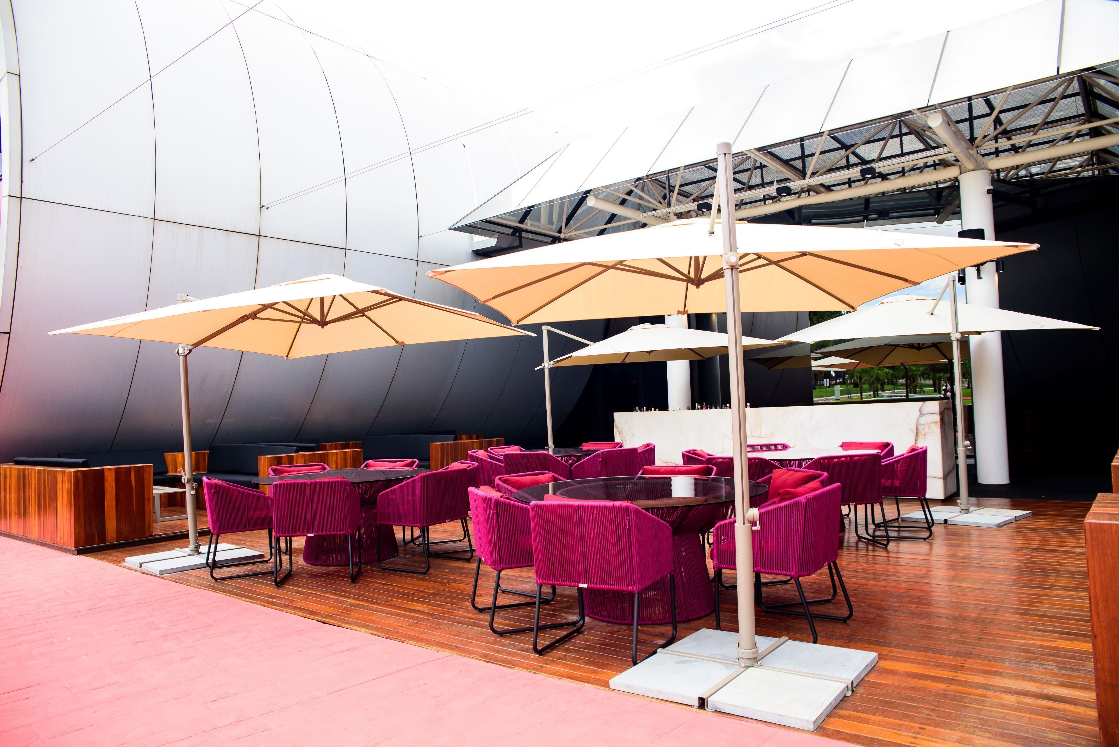 Un espace de restauration extérieur moderne, doté d’un plancher en bois, de chaises roses et de grands parasols.
