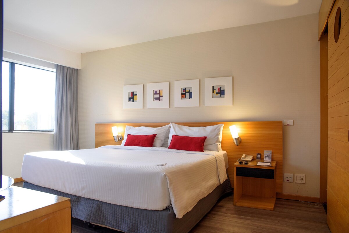 Une chambre d’hôtel avec un grand lit, deux tables de chevet, un bureau et une fenêtre avec des rideaux.