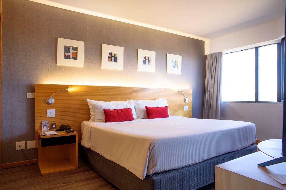 Una habitación de hotel con una cama grande, mesitas de noche, un escritorio y una ventana con cortinas.