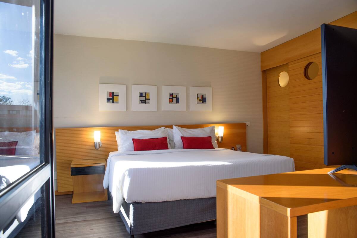 Una habitación de hotel con cama, mesitas de noche, escritorio y obras de arte en la pared.