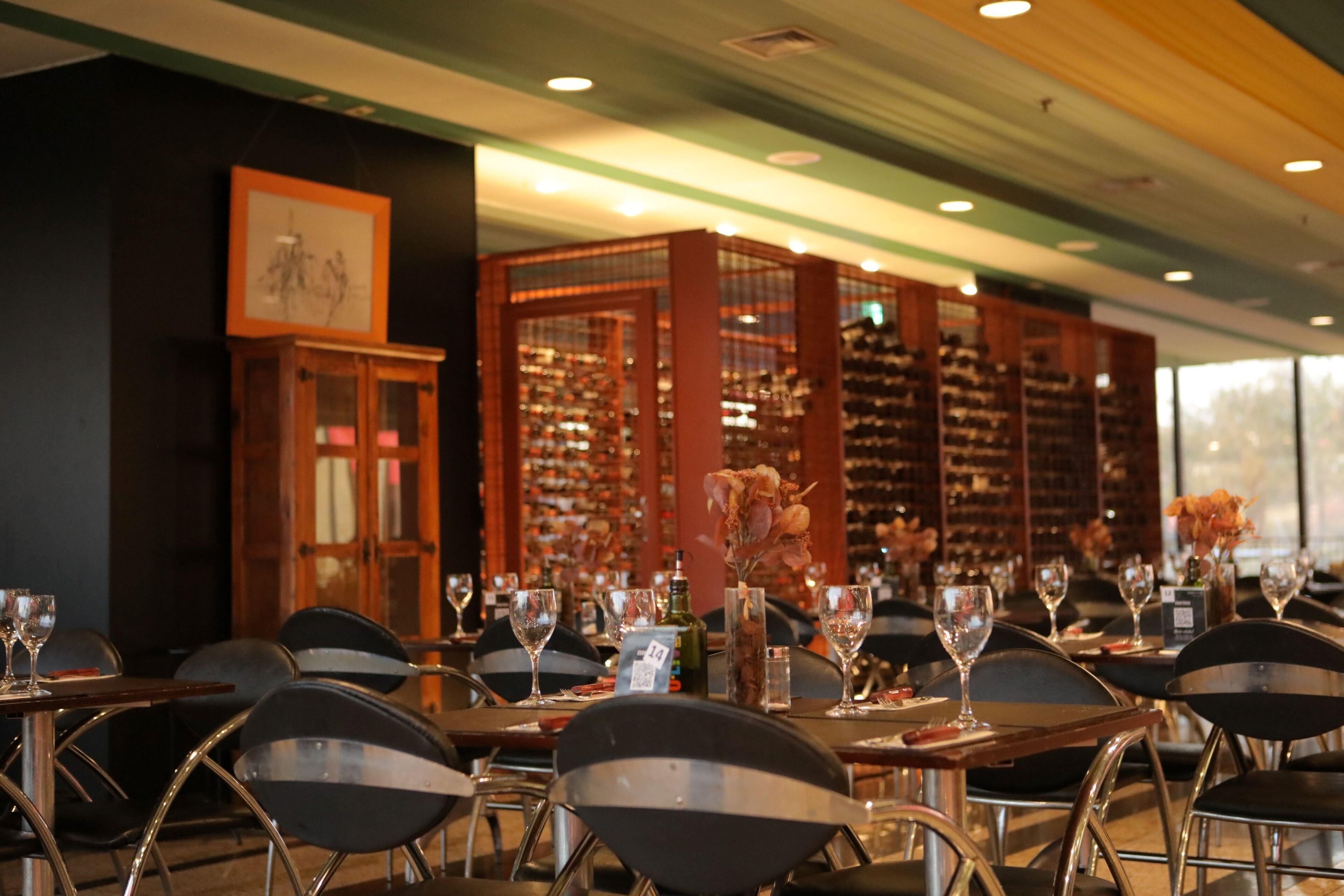 Een restaurantinterieur met gedekte tafels, stoelen en een wijnrek op de achtergrond.