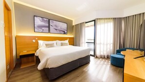 Ein Hotelzimmer mit einem großen Bett, einem Schreibtisch und einem Sessel. Über dem Bett befinden sich zwei an der Wand befestigte Kunstwerke.
