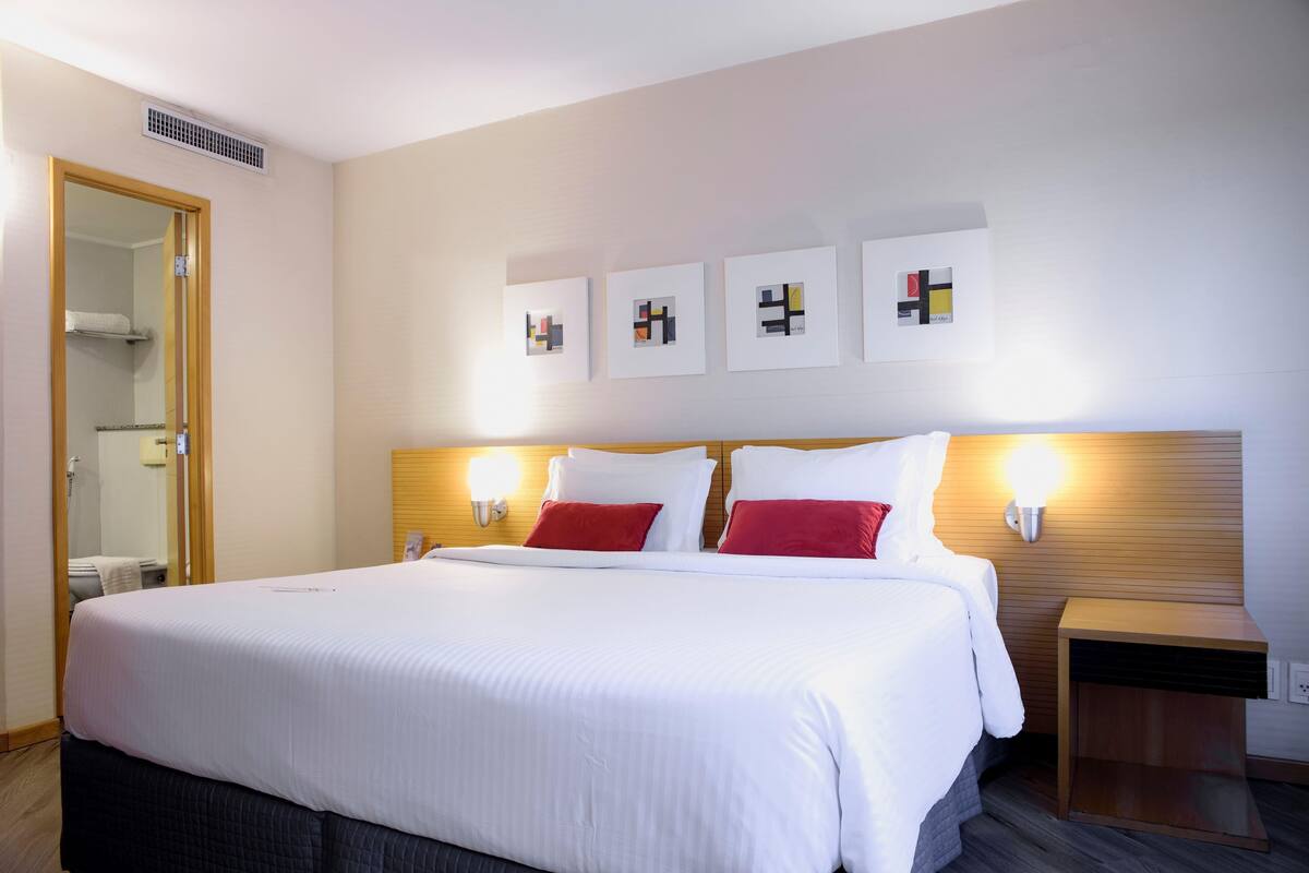 Habitación de hotel con una cama grande, dos mesitas de noche, un cabecero de madera y tres obras de arte colgadas en la pared.