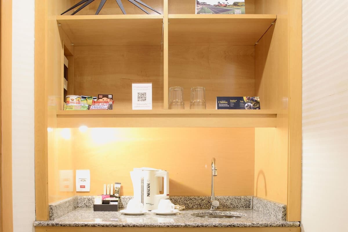 Una kitchenette compacta con refrigerador integrado, una encimera con cafetera y un lavamanos pequeño.
