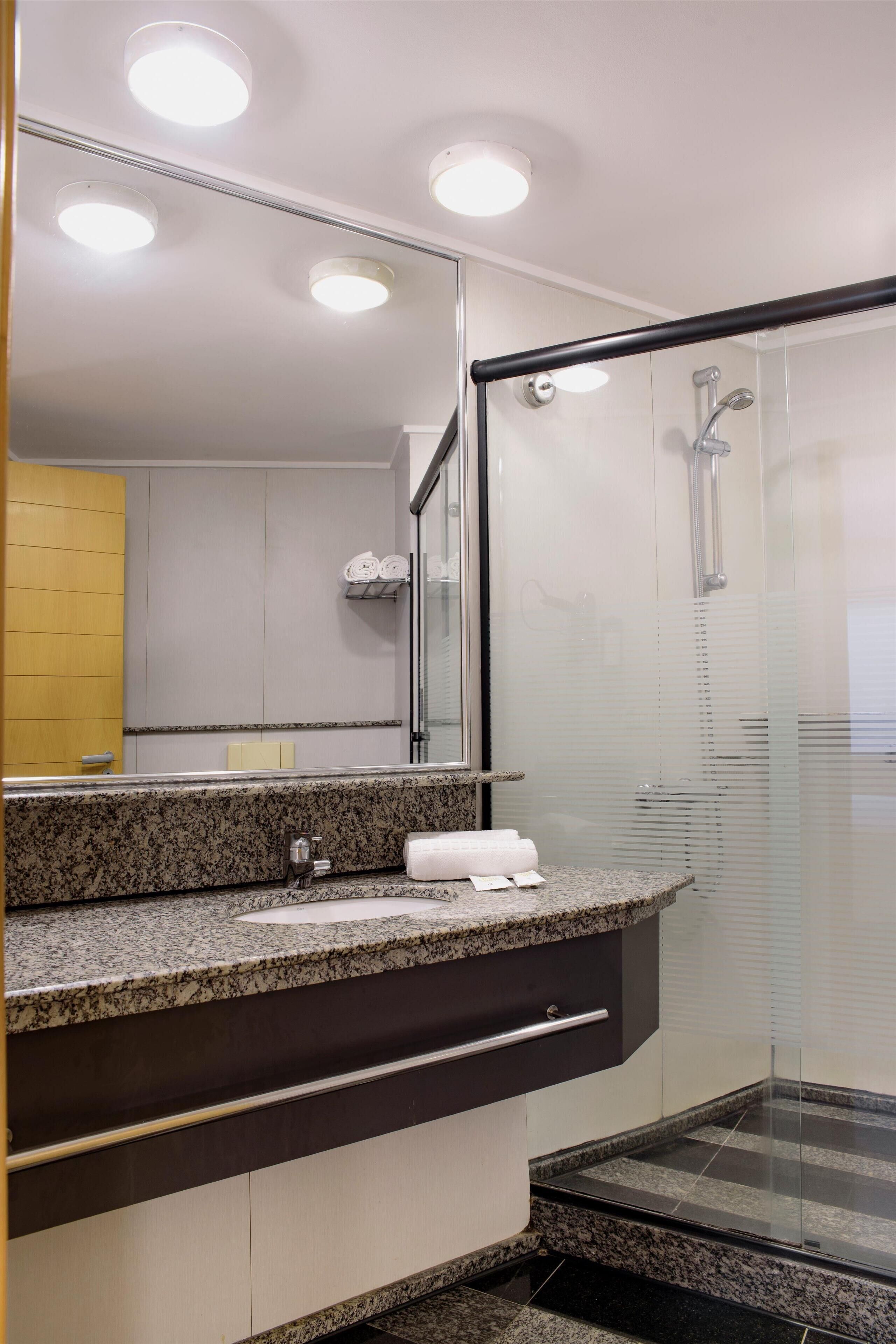 Une salle de bain moderne avec un comptoir en granit, une cabine de douche en verre et un grand miroir.