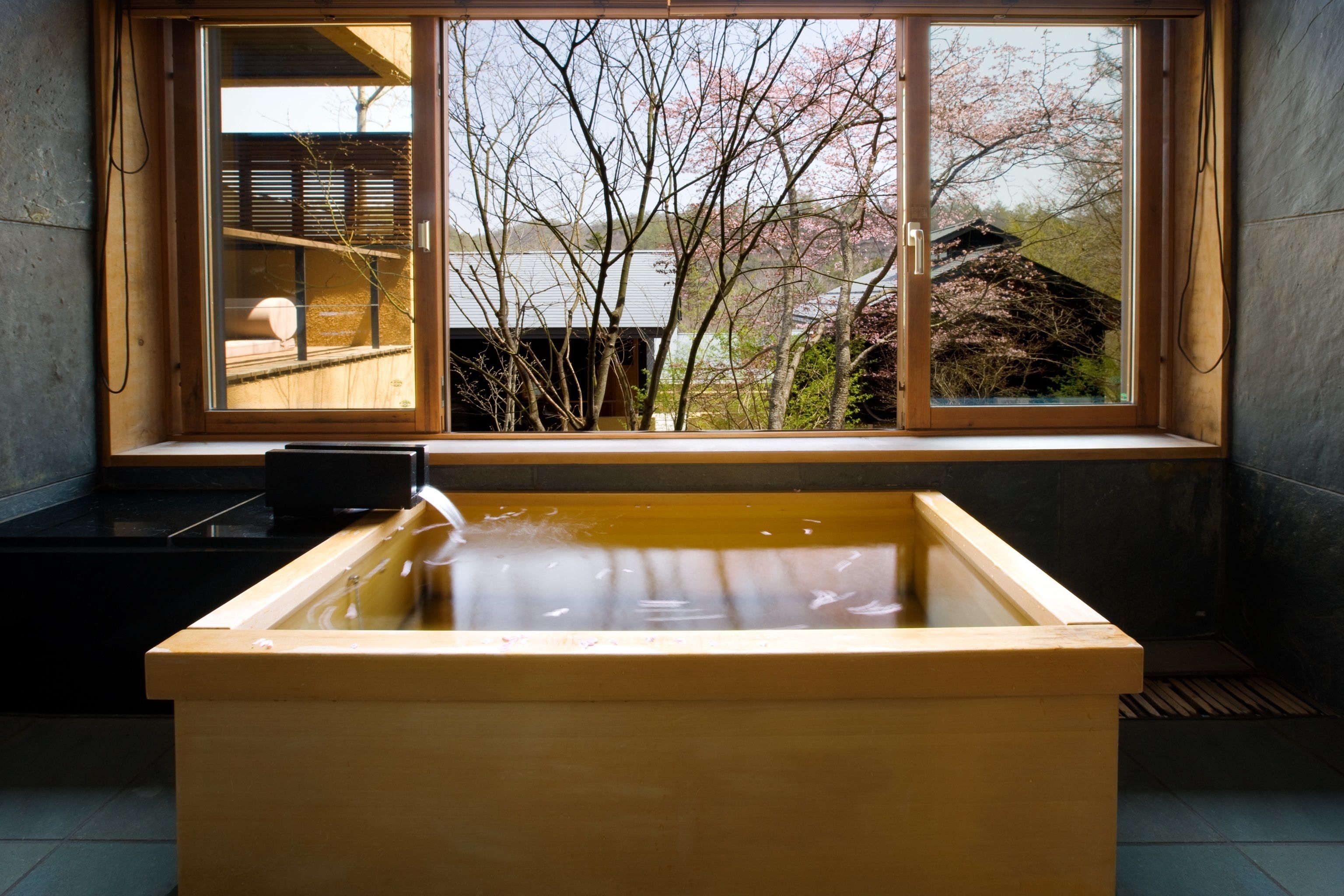A wooden bathtub with a view of cherry blossoms through a large window.