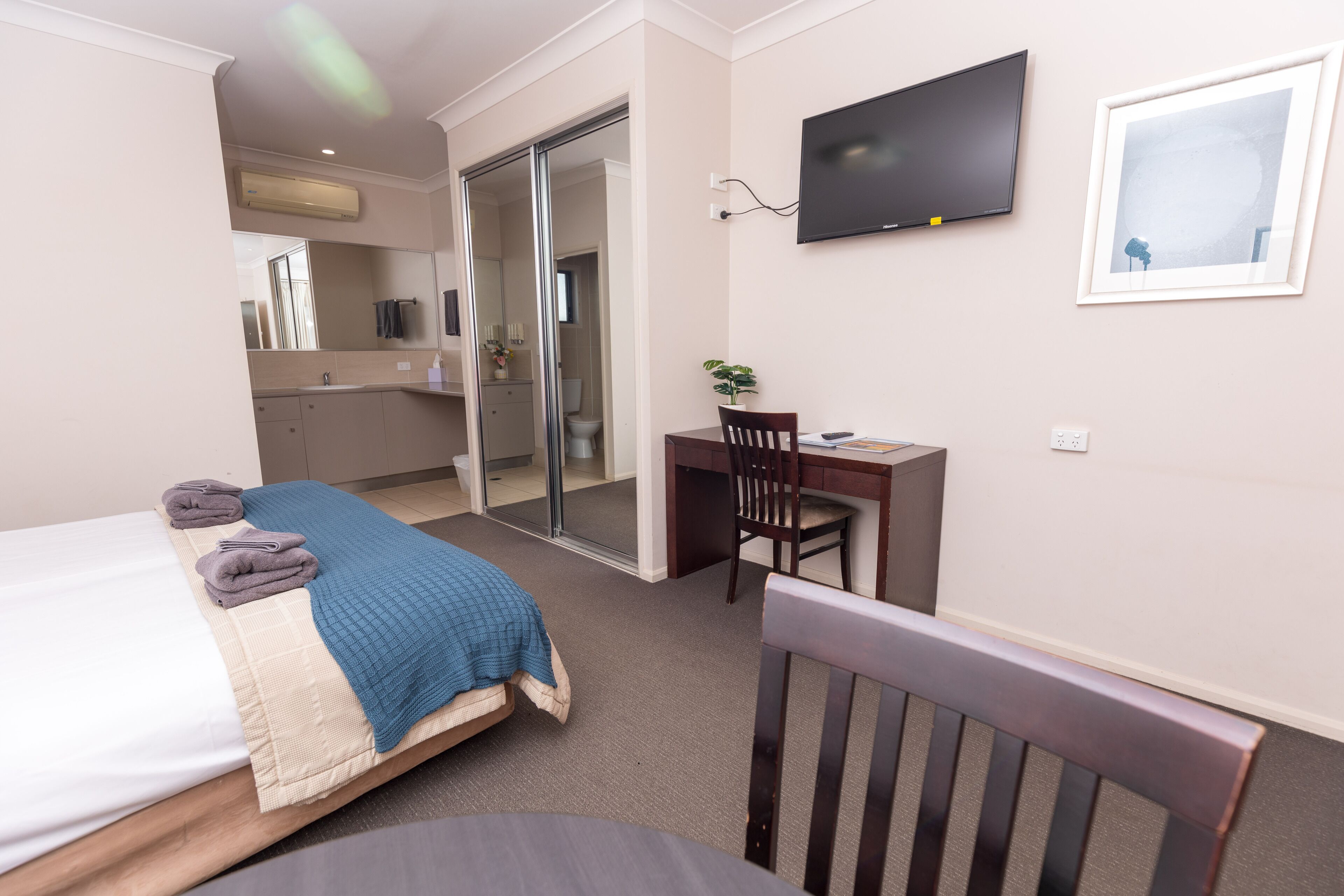 A bedroom with a bed, a desk, a chair, a TV, and a sliding door to a bathroom.