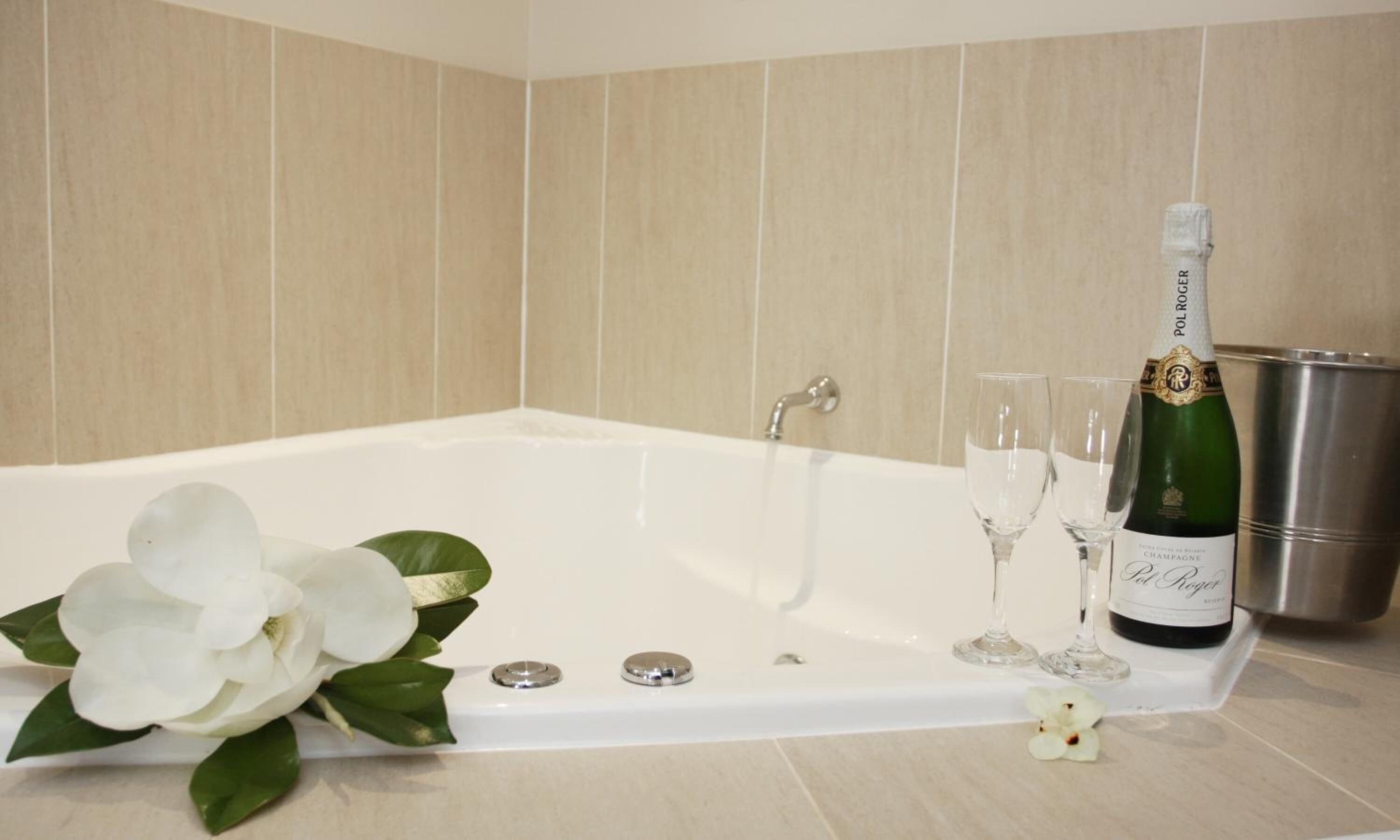A bathroom with a bathtub, a champagne bottle, and two glasses.