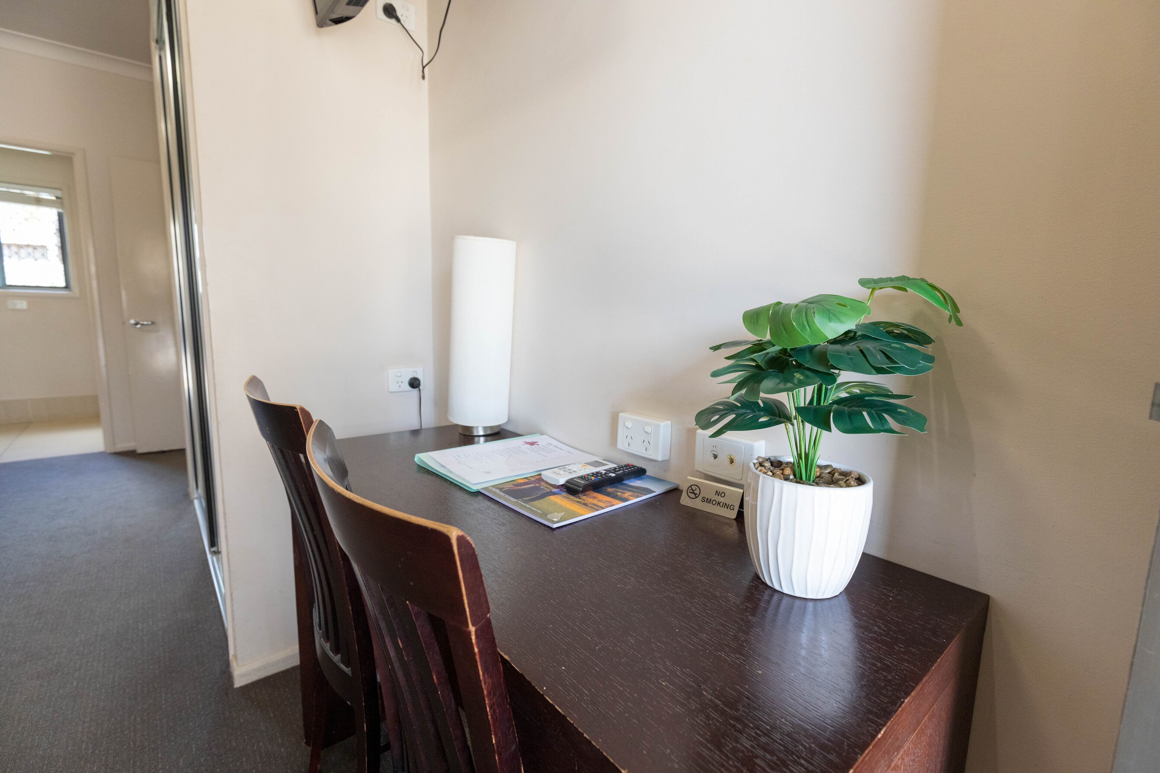 A dining area with a wooden table, chairs, a potted plant, a remote control, and a 'No Smoking' sign.