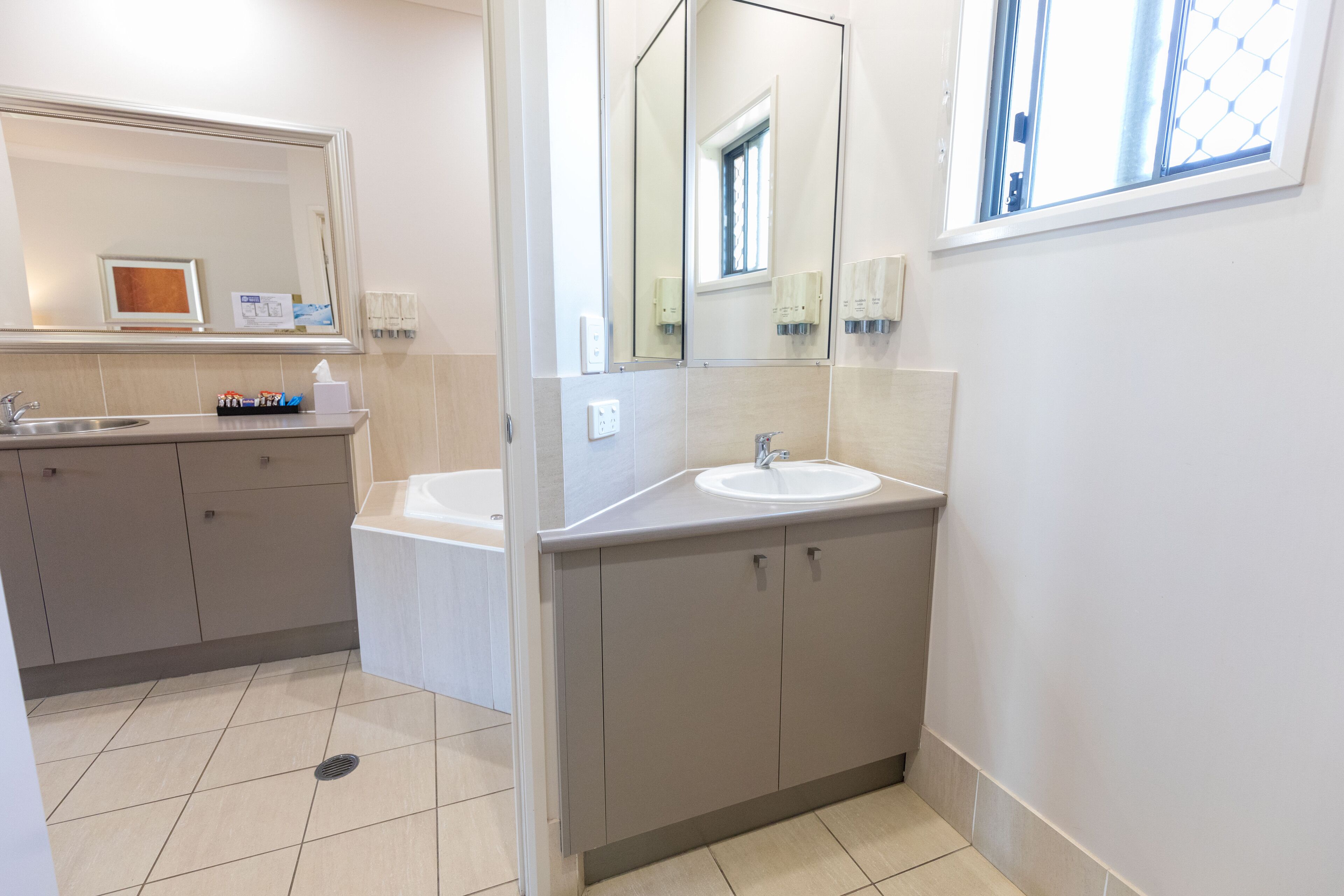 A modern bathroom with two sinks, a large mirror, and a window.