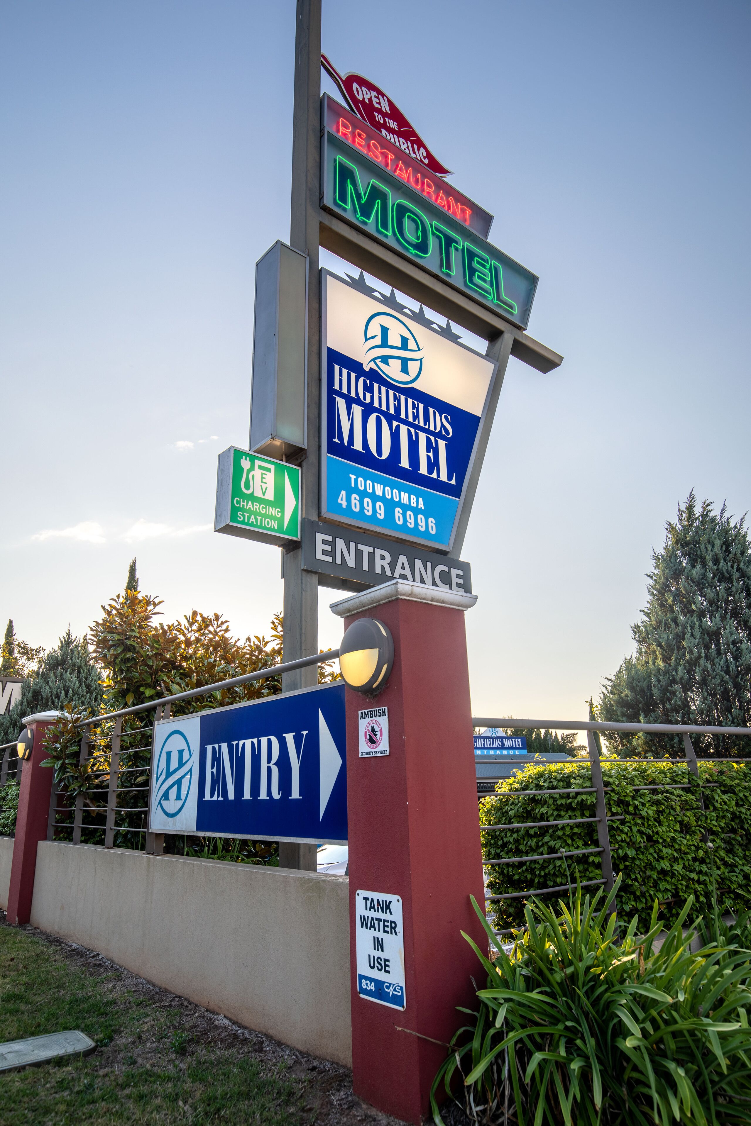 A motel sign with a restaurant sign above it, an entry sign, and a charging station sign.