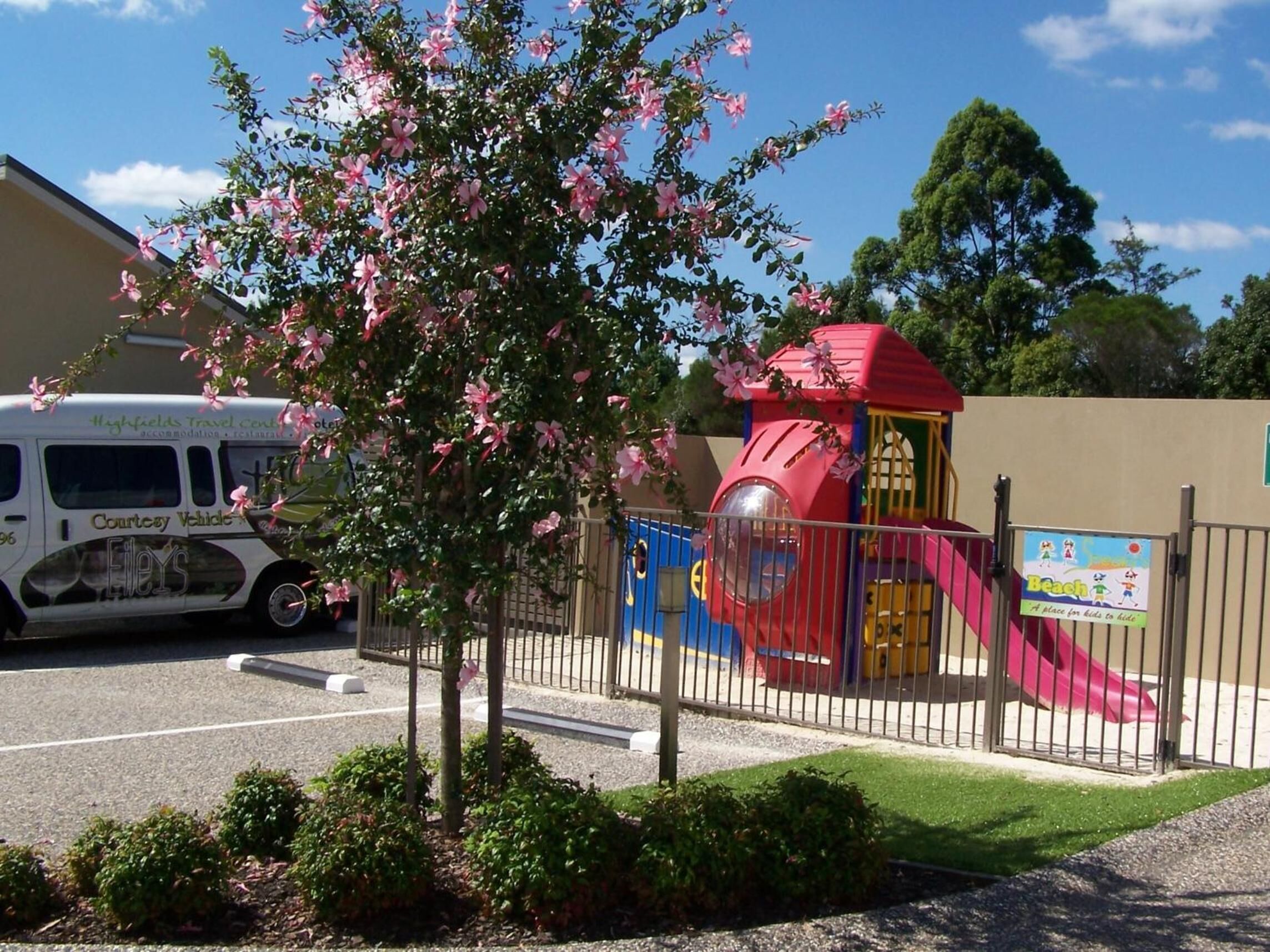 A playground with a slide and climbing structures, a bus, and a building with signage.
