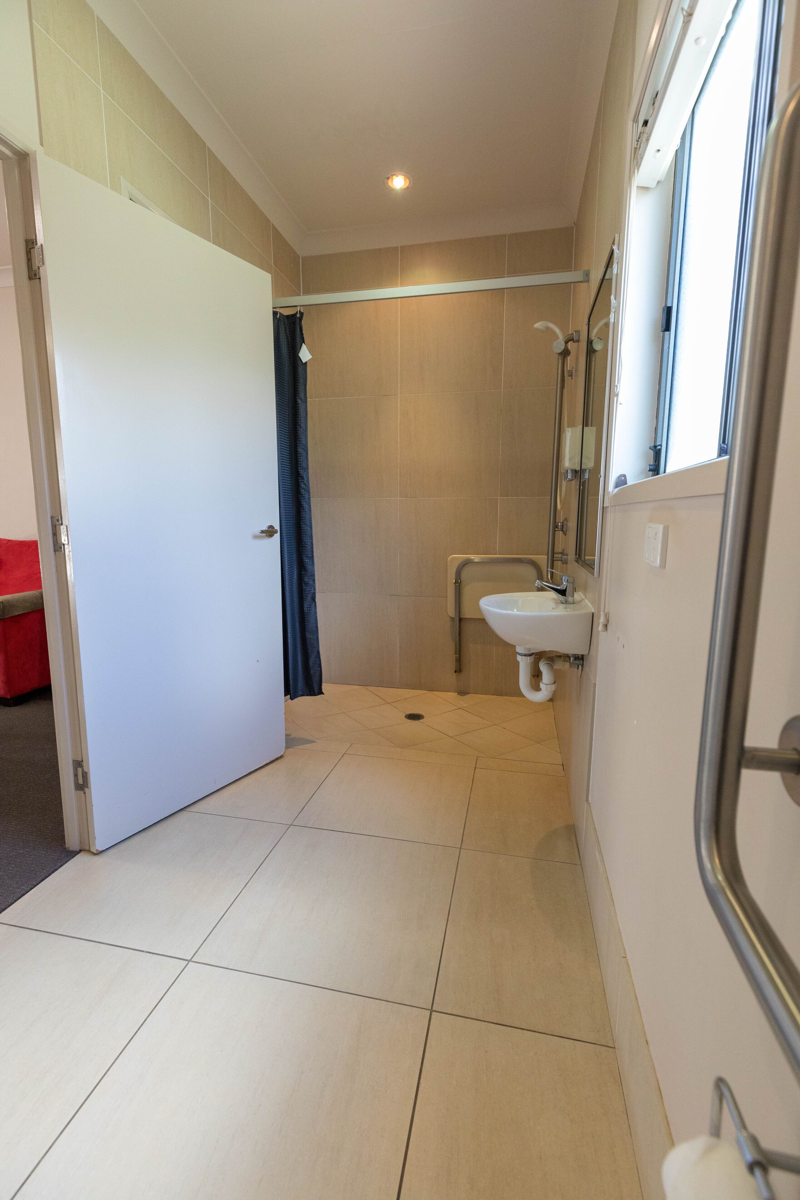 Un baño estrecho con ducha, lavabo y puerta que da a otra habitación.