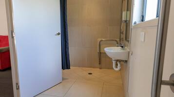 Un baño estrecho con ducha, lavabo y puerta que da a otra habitación.