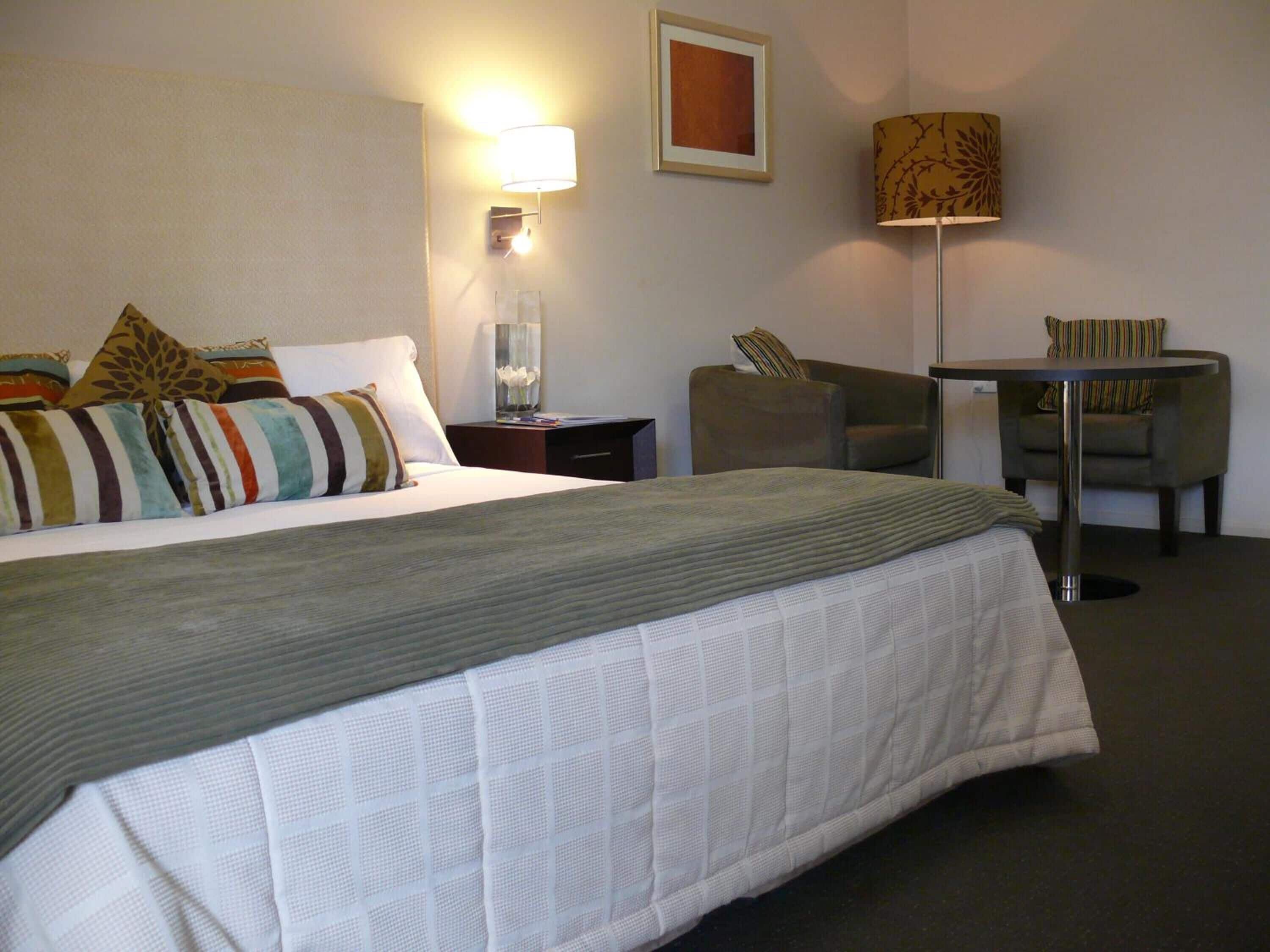 A hotel room with a large bed, a desk, a chair, a lamp, and a framed picture on the wall.