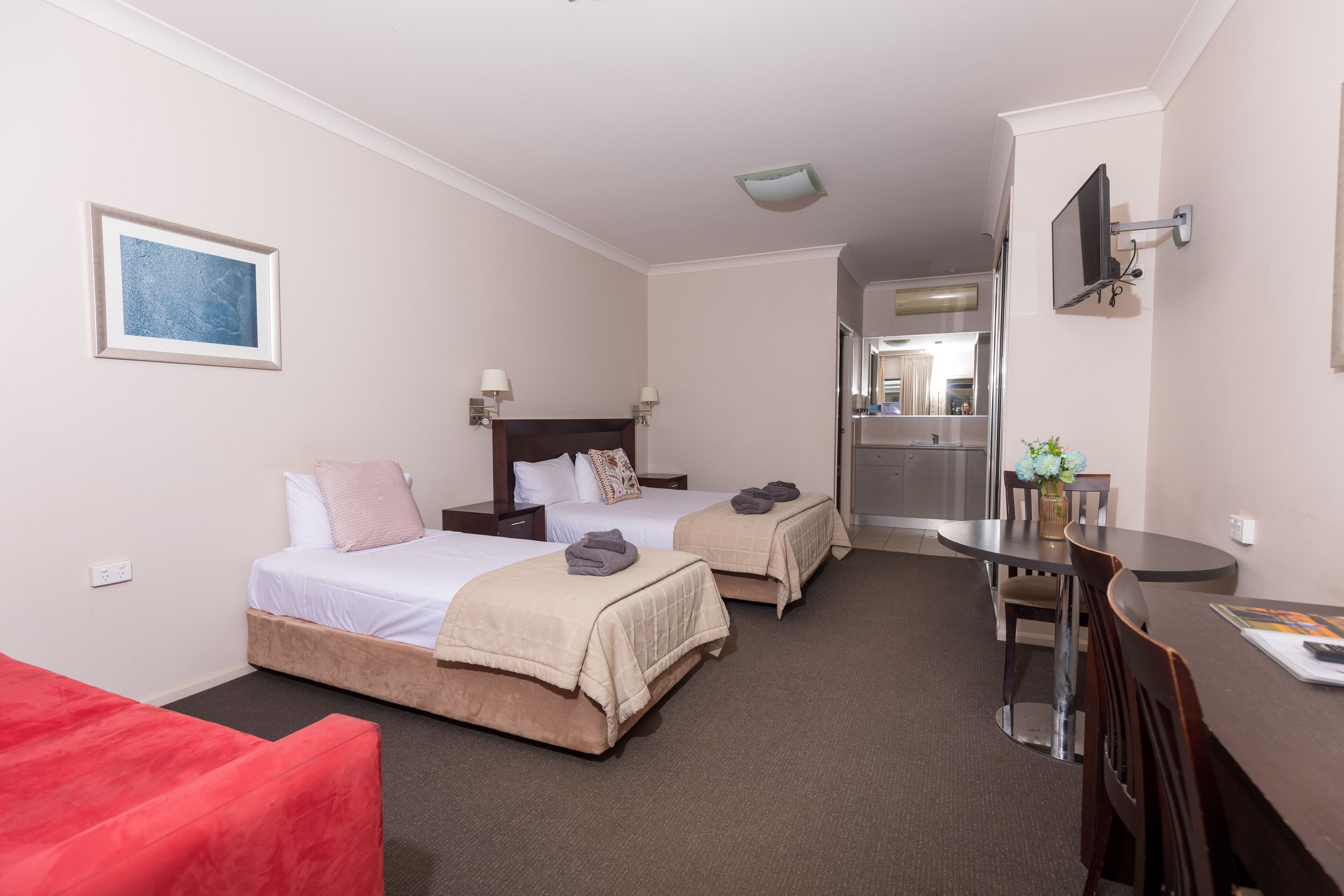 A hotel room with two beds, a desk, a chair, a TV, and a bathroom visible through an open door.