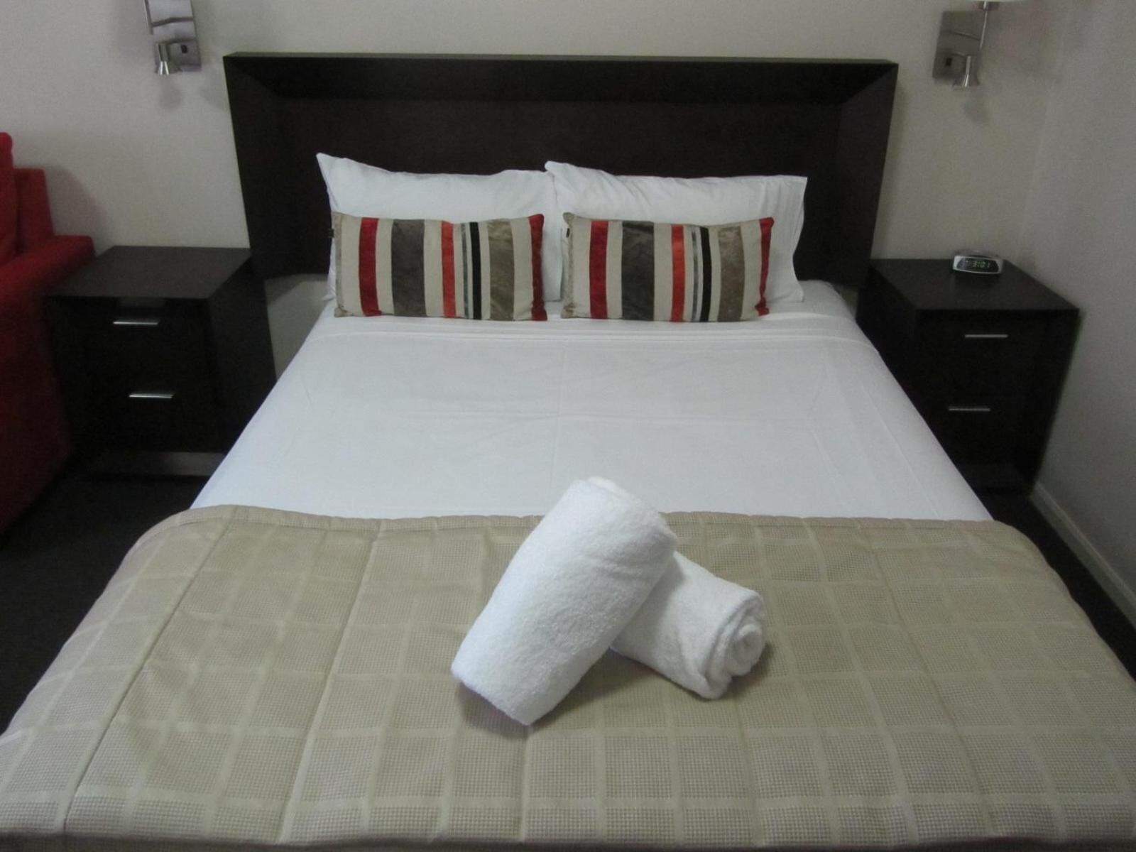 A neatly made bed with a white duvet, two striped pillows, and a folded white towel on a beige bedspread.