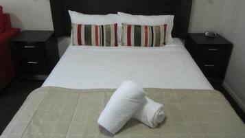 A neatly made bed with a white duvet, two striped pillows, and a folded white towel on a beige bedspread.