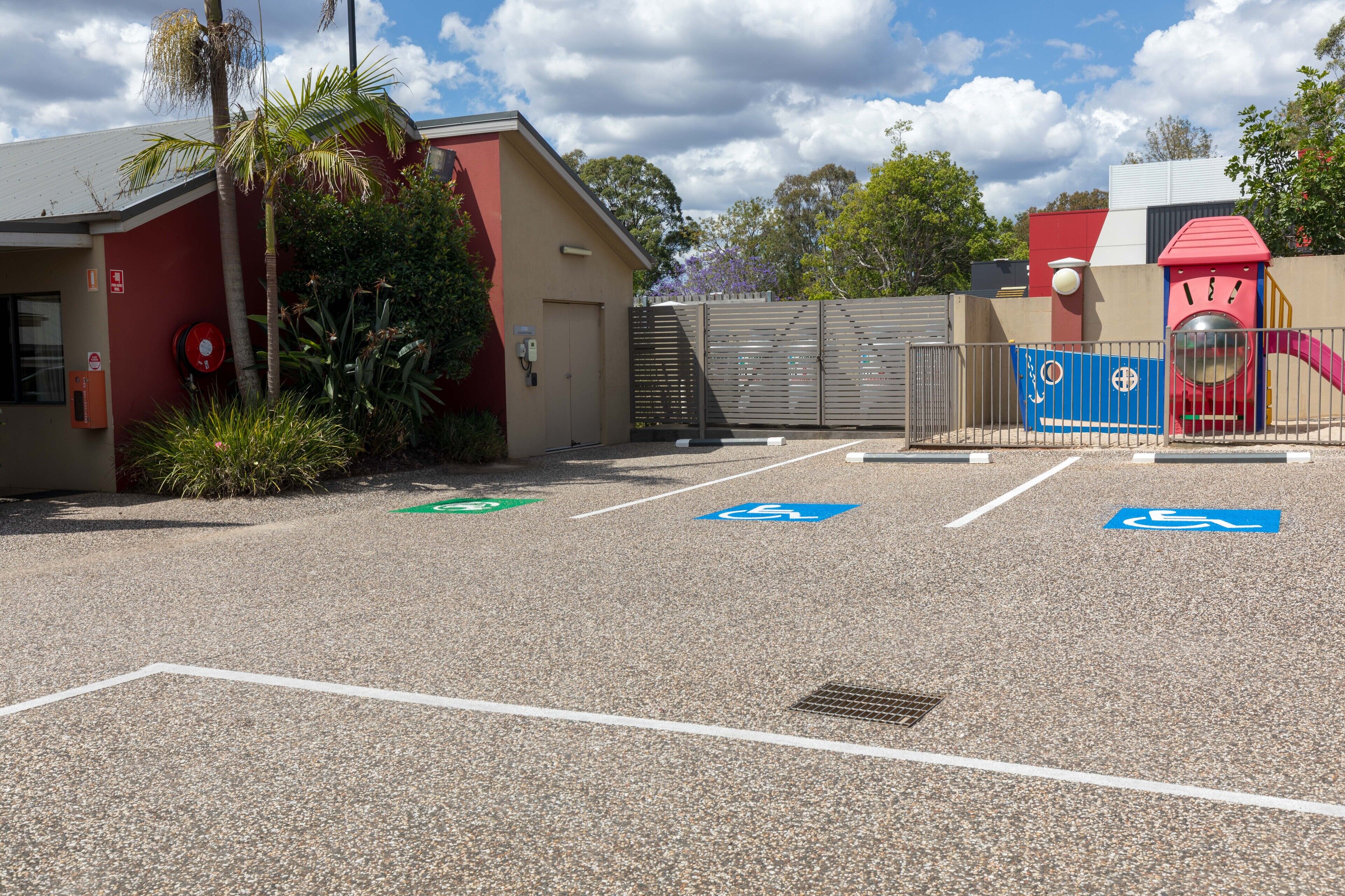 A parking area with handicapped accessible spaces, a red building, and a playground structure.