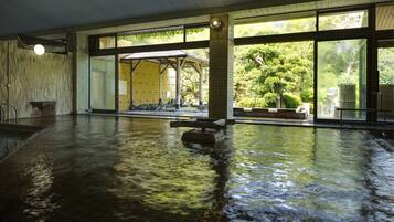 Piscina interior con agua cristalina, grandes ventanales y zona cubierta con asientos.