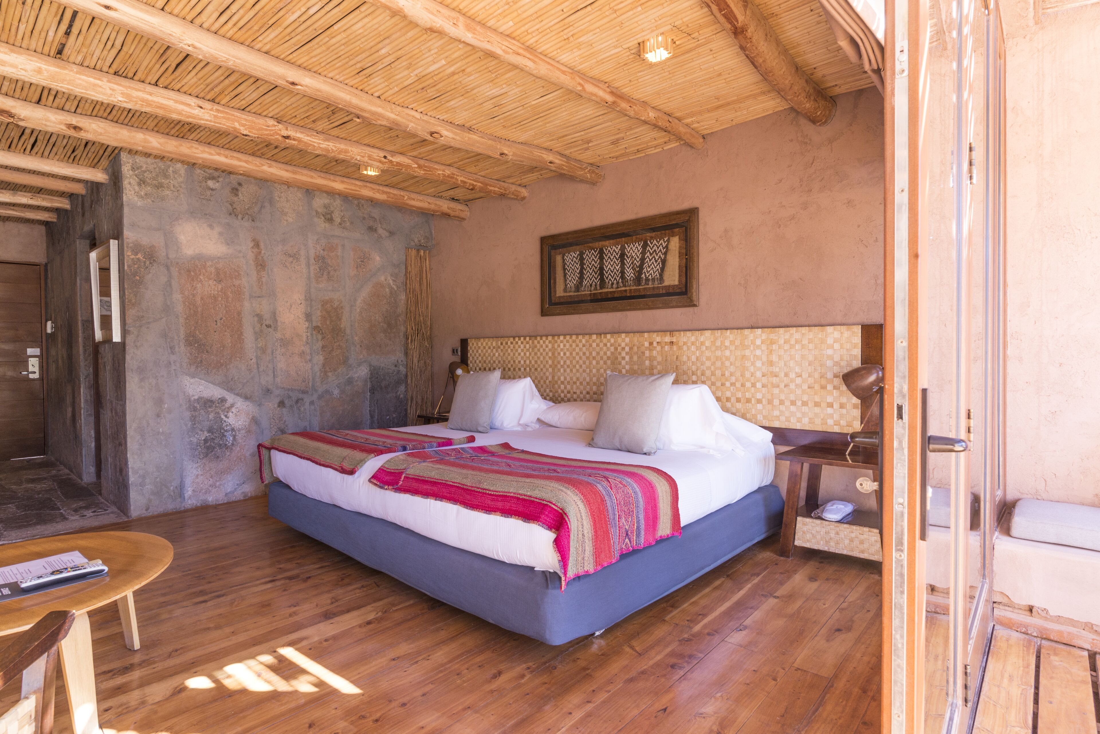 A bedroom with a large bed, wooden floor, stone walls, and a wooden ceiling.