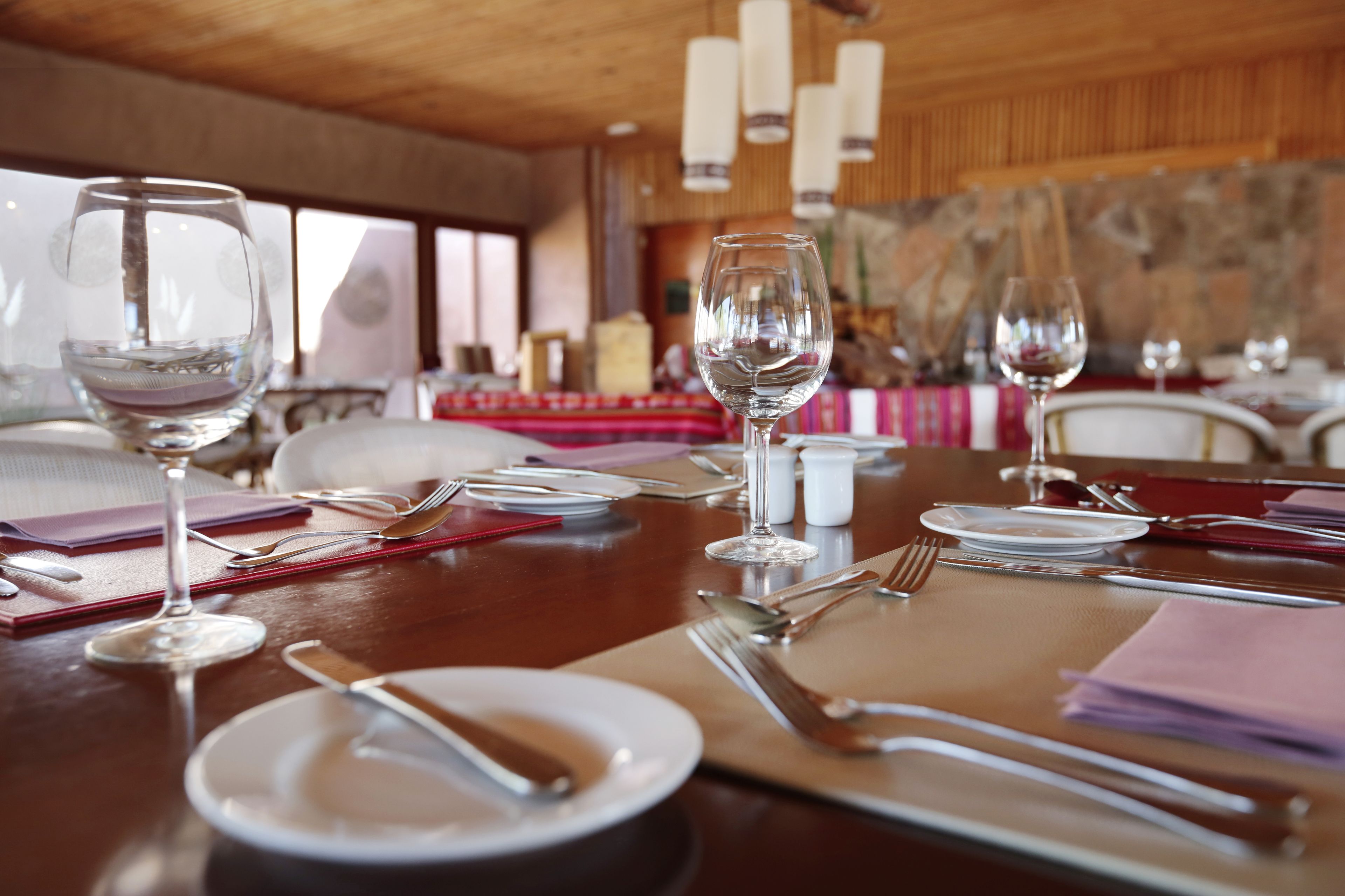 Mesa lista para comer, con copas de vino, platos, cubiertos y servilletas en un restaurante con decoración de madera y paredes de piedra.