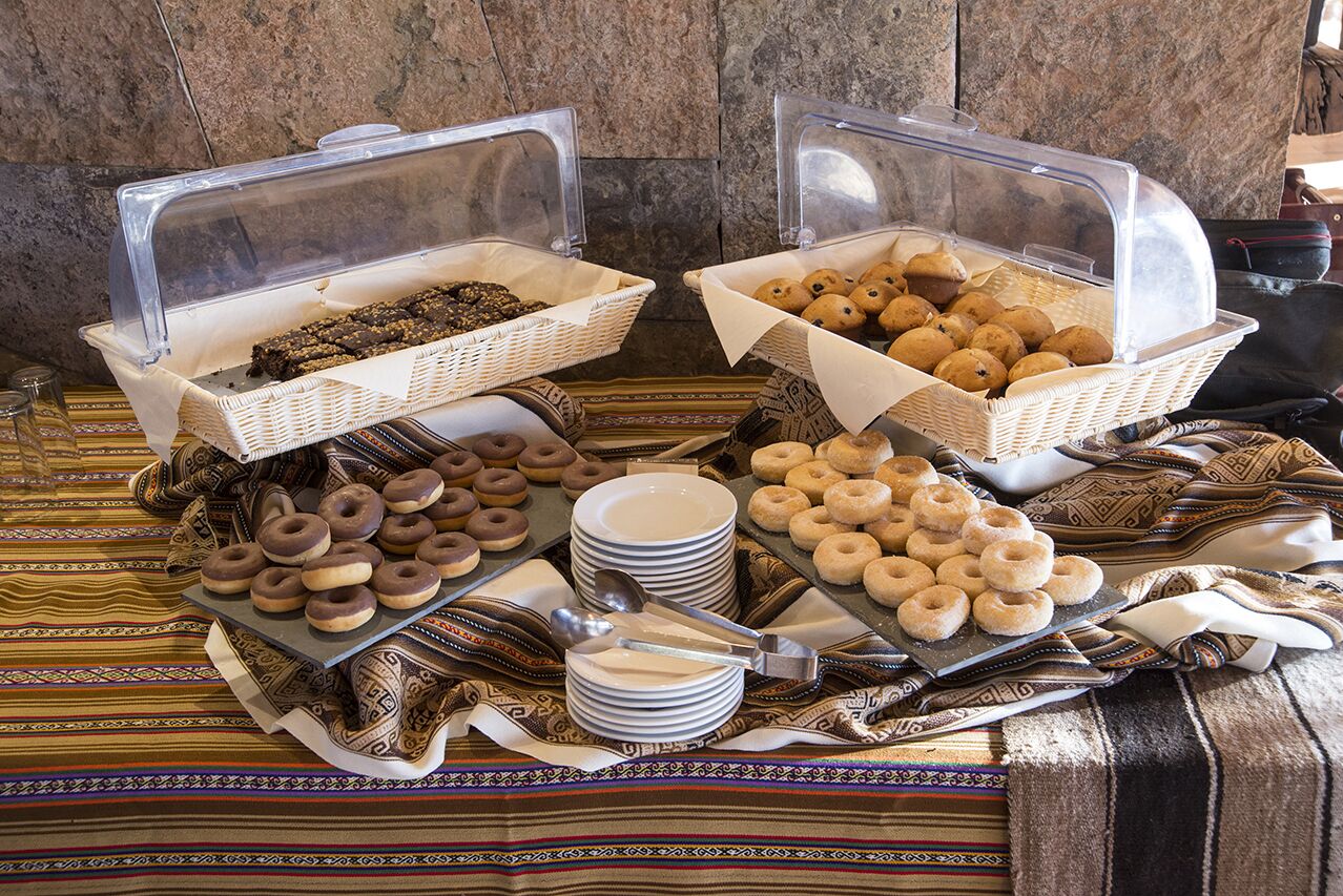 A buffet with various baked goods and pastries, including donuts and muffins, arranged on a table with a patterned tablecloth.