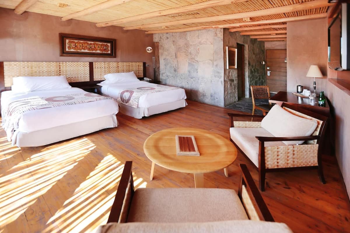 A room with two beds, a round wooden table, and a chair.