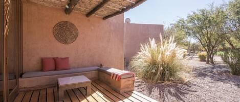 An outdoor patio with a wooden deck, a cushioned seating area, and a decorative wall.
