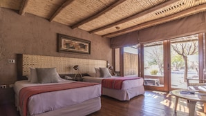 A room with two beds, a wooden ceiling, a large window, and a small table.