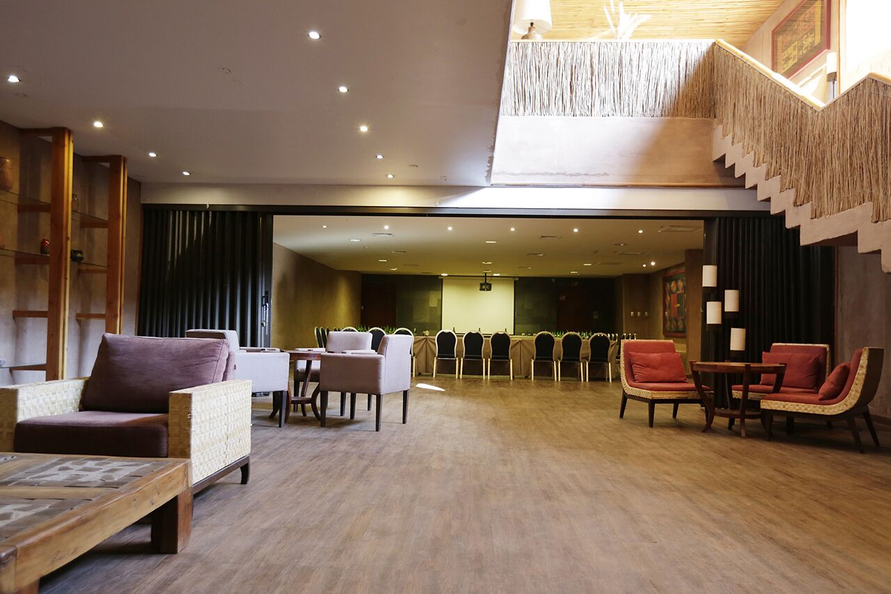 Un lobby espacioso con techo alto, una escalera de diseño único y un área de estar con sillas y mesas.