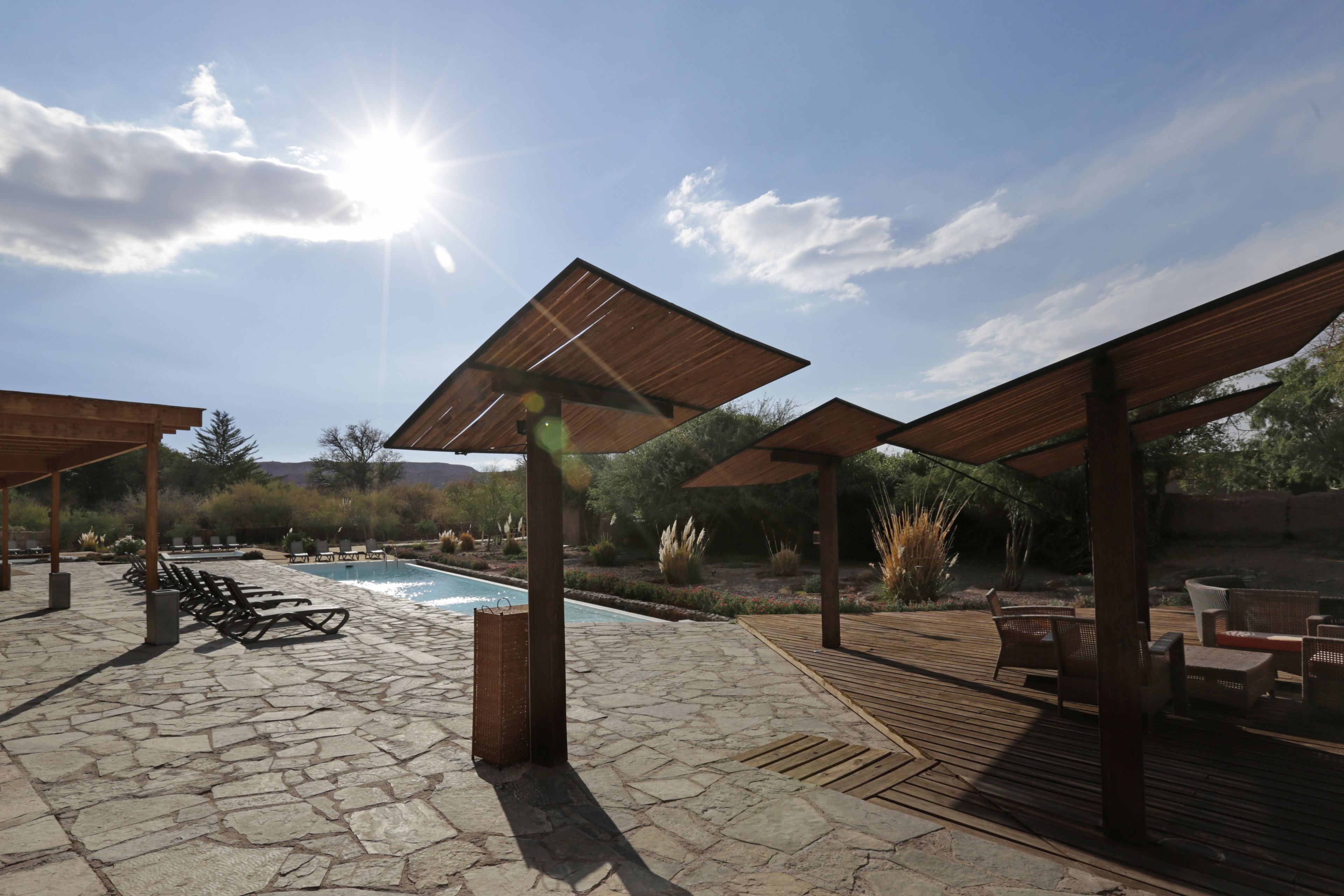 Ein Poolbereich mit Steinböden, Holzpergolen, Liegestühlen und einem Pool.