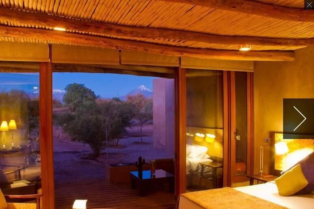 A room with a bed, a desk, and a view of a mountain.