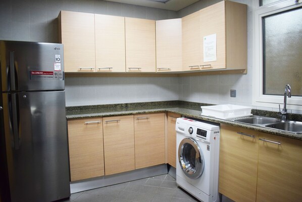 Una cocina compacta con armarios de madera, un refrigerador de acero inoxidable, una lavadora y un lavamanos doble.