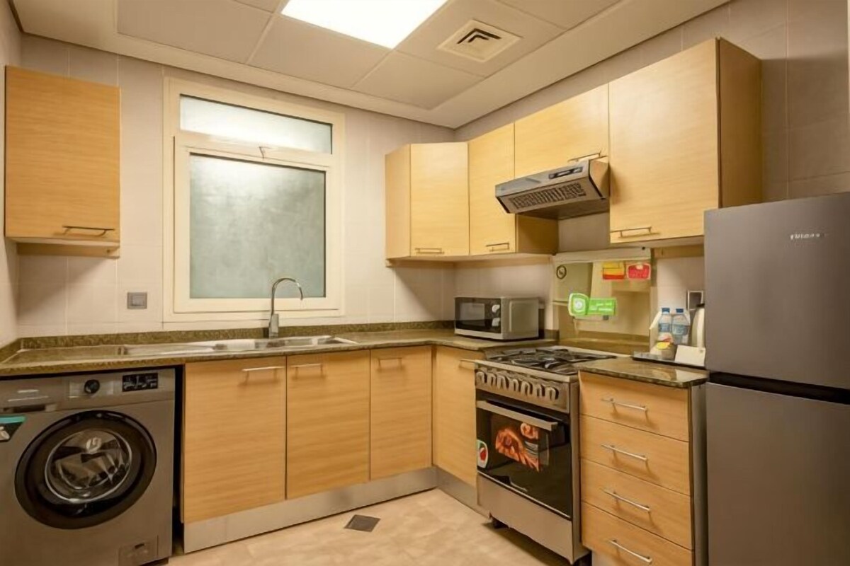 Una cocina compacta con muebles de madera, microondas, estufa, lavadora y refrigerador.