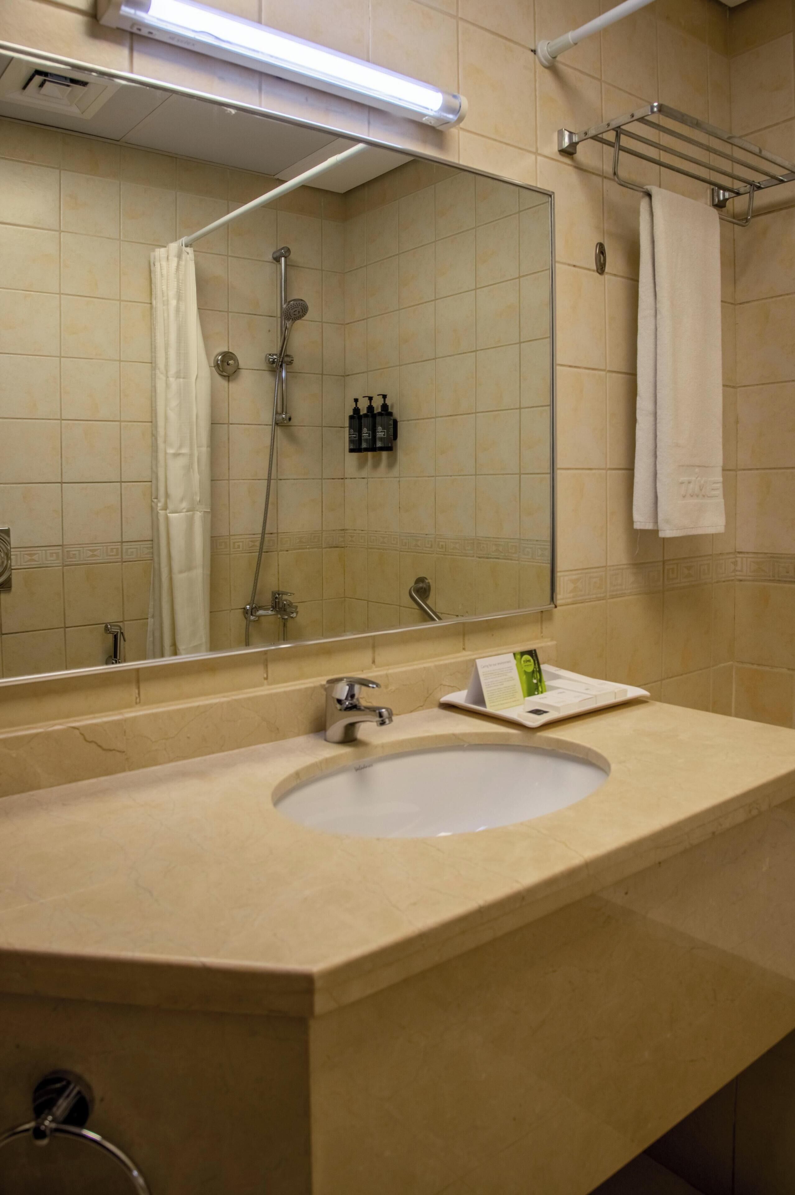 A bathroom with a large mirror, a sink, a shower, and a towel rack.
