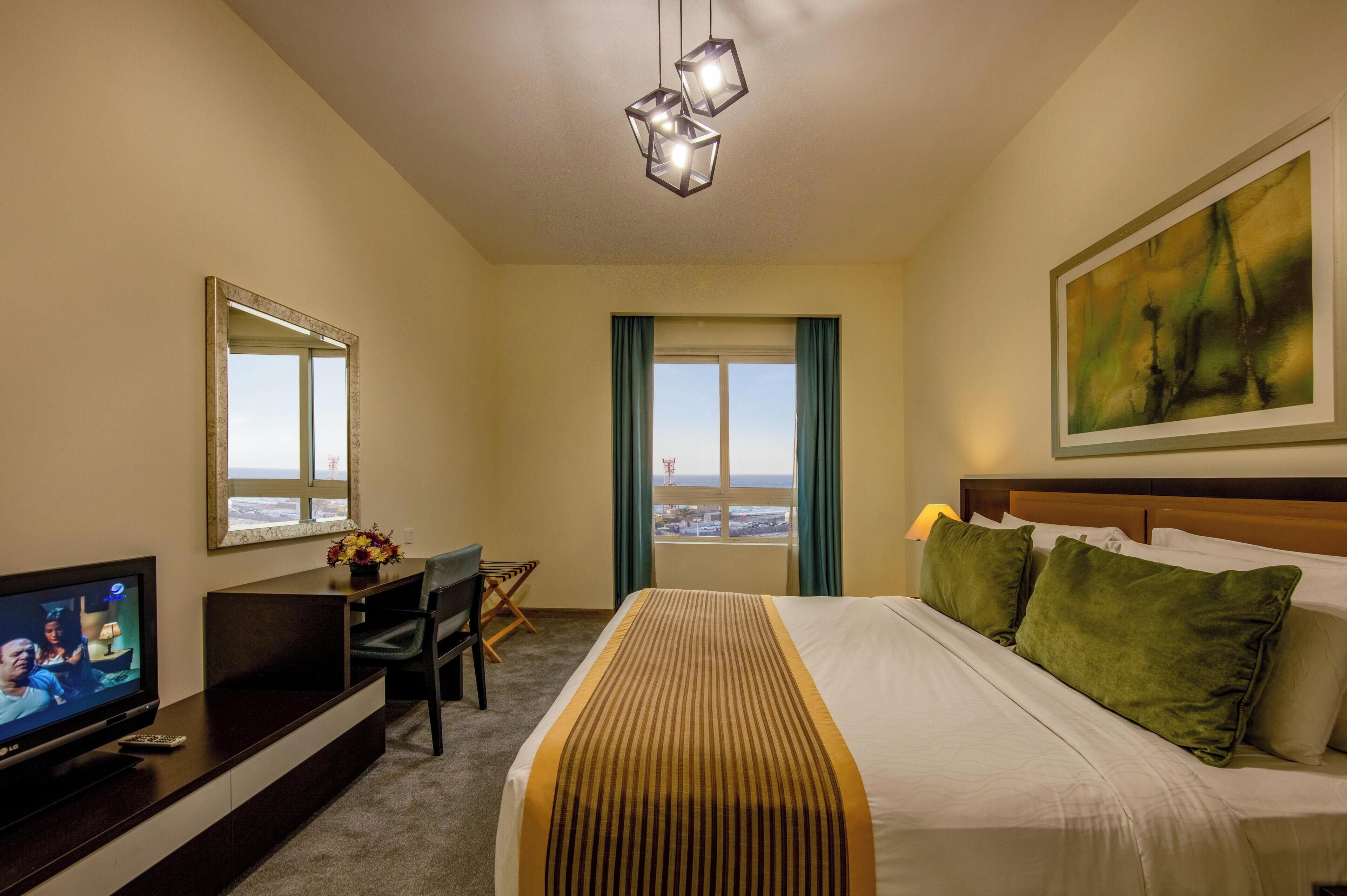 Habitación de hotel con cama, escritorio, televisor, ventana con vista y un cuadro en la pared.