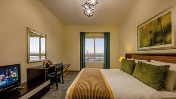 Habitación de hotel con cama, escritorio, televisor, ventana con vista y un cuadro en la pared.