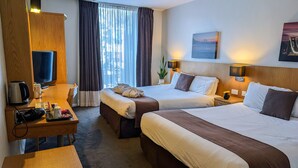 Habitación de hotel con dos camas, un escritorio con cafetera, televisión y un ventanal grande con cortinas.
