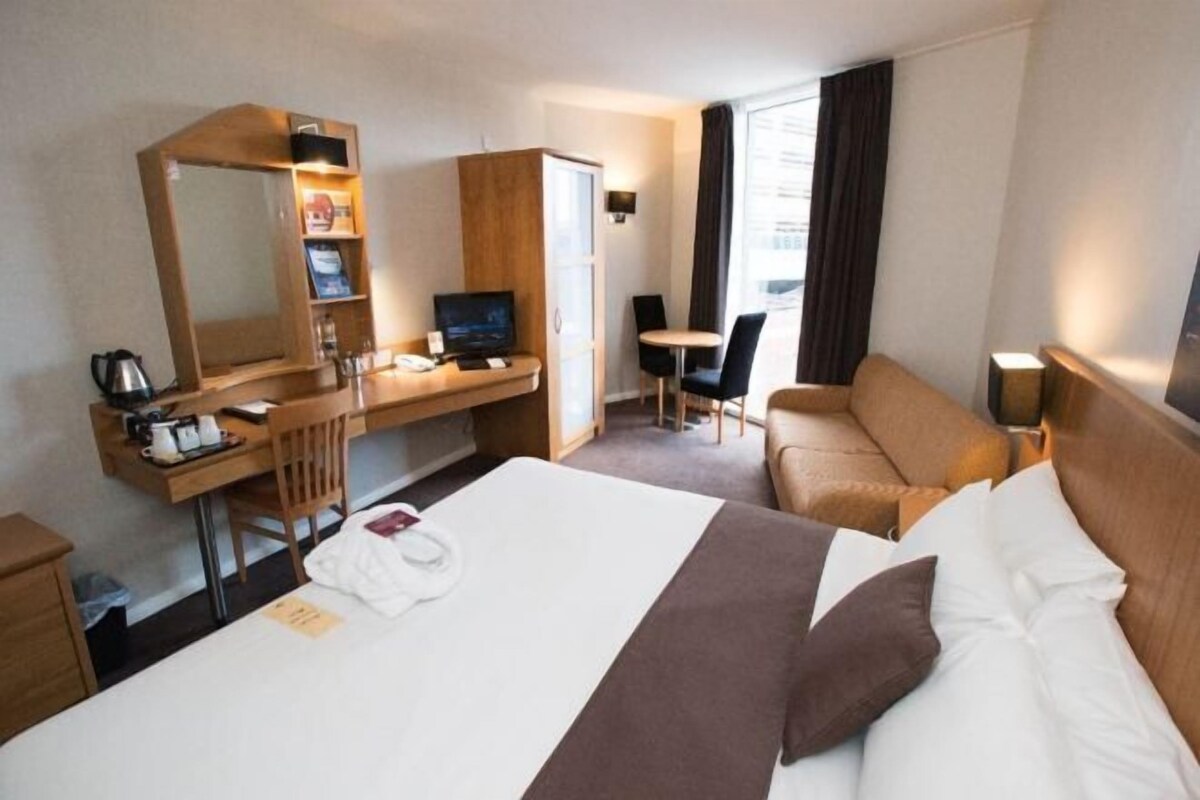 Habitación de hotel con cama, escritorio, computadora, una silla, sofá y un espejo grande.