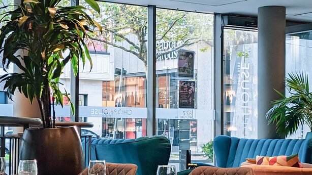 Un restaurante con un ventanal grande, una planta en maceta y una zona de estar con sillas acolchadas y una mesa.