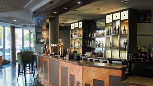 Una zona de bar con barra, taburetes y estantes llenos de botellas y vasos.