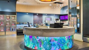 Modernilla designilla sisustettu vastaanottoaula, jossa on keskeisellä paikalla sijaitseva palvelutiski, digitaalinen näyttö ja oleskelualue, josta on näkymä vastaanottotiskin suuntaan.