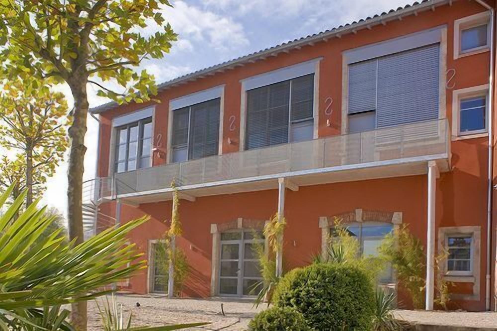 Un edificio de dos pisos con fachada roja, múltiples ventanas y un corredor cubierto.
