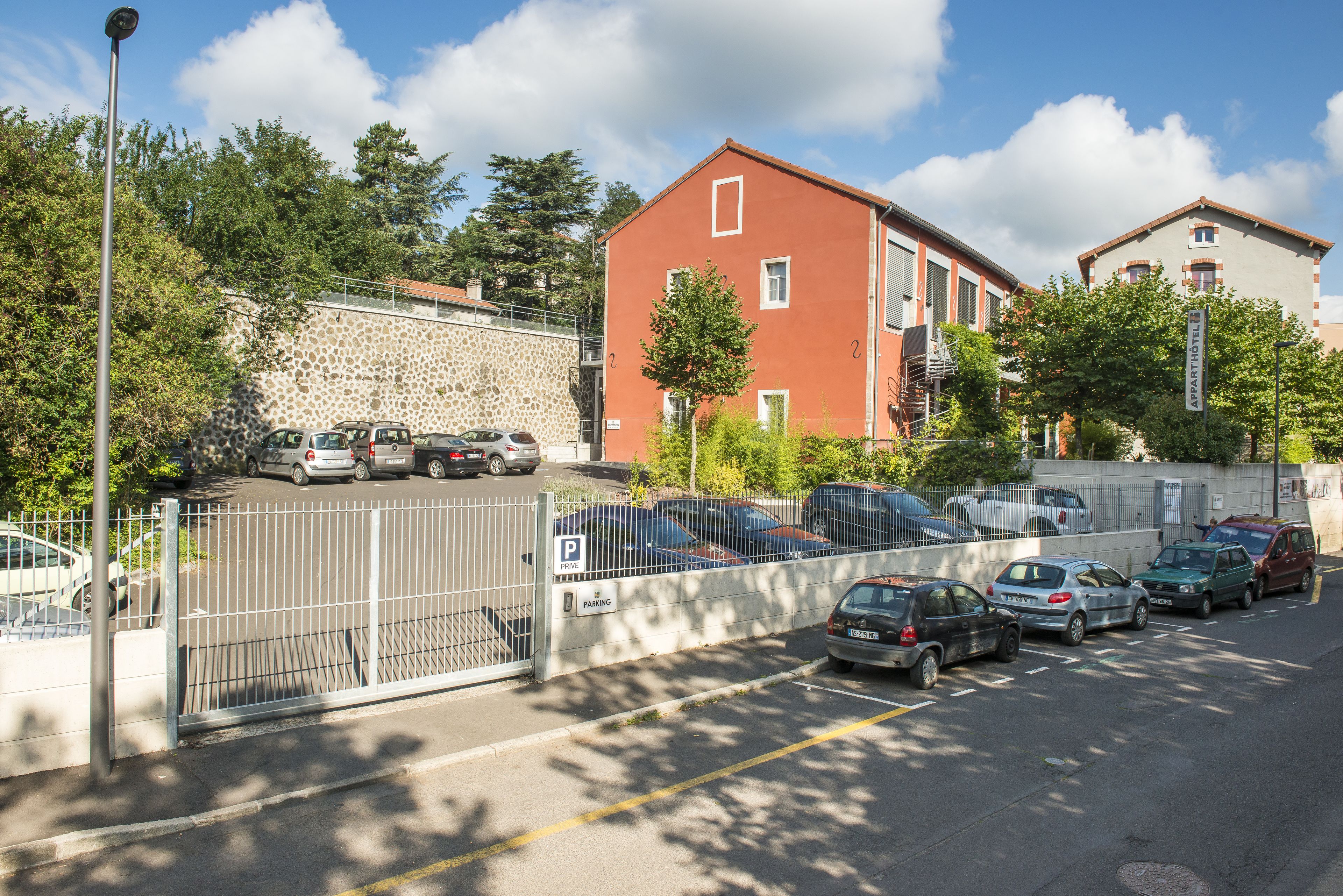 A parking lot with several cars, a stone wall, and a red building with multiple windows.