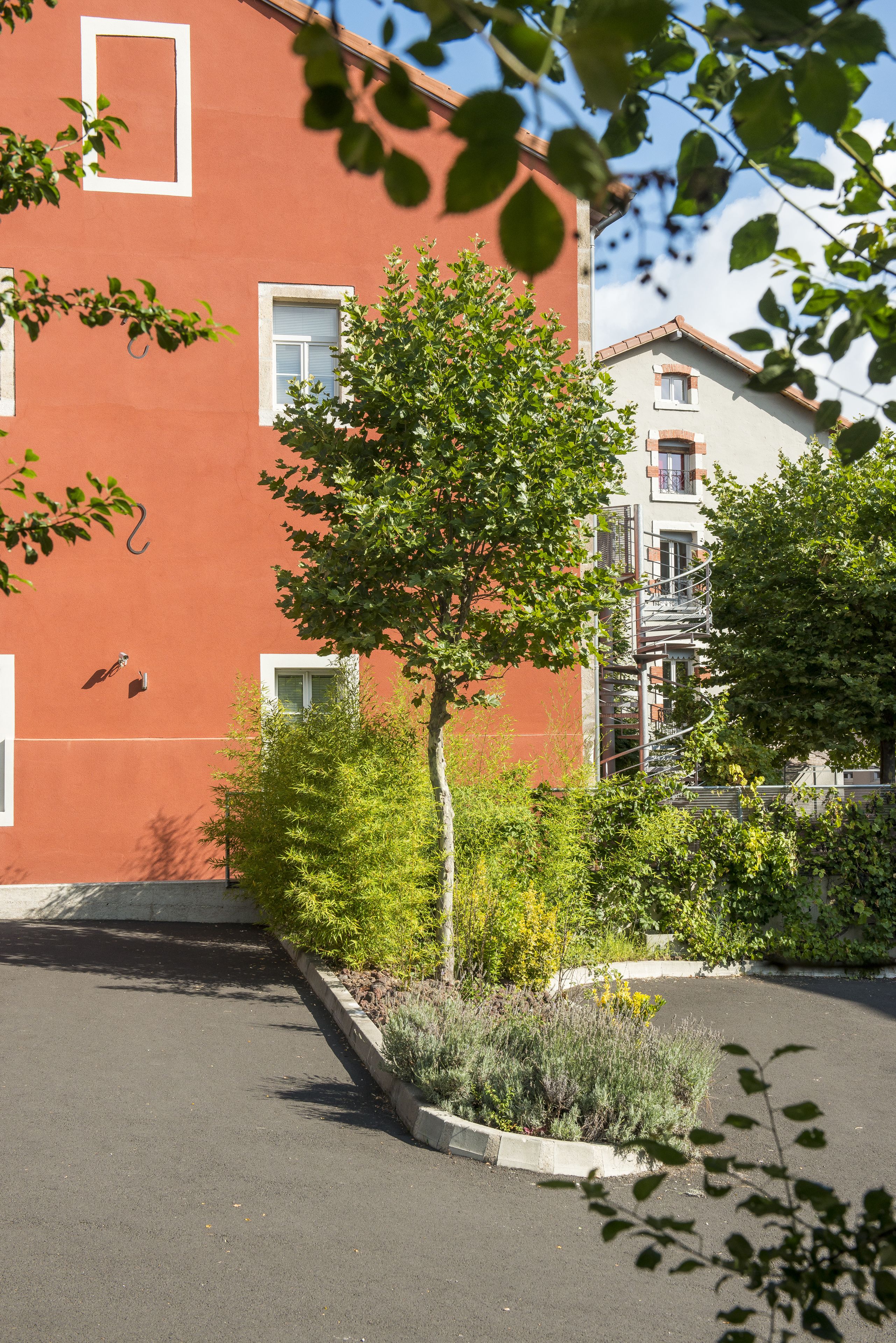 A building with a red facade, multiple windows, and a small tree in the foreground.
