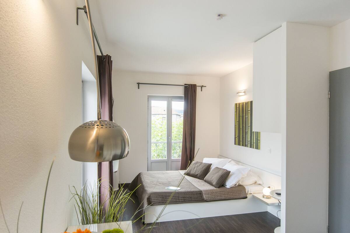 Une chambre d’hôtel moderne, équipée d’un lit, d’une table de chevet et d’une grande fenêtre.