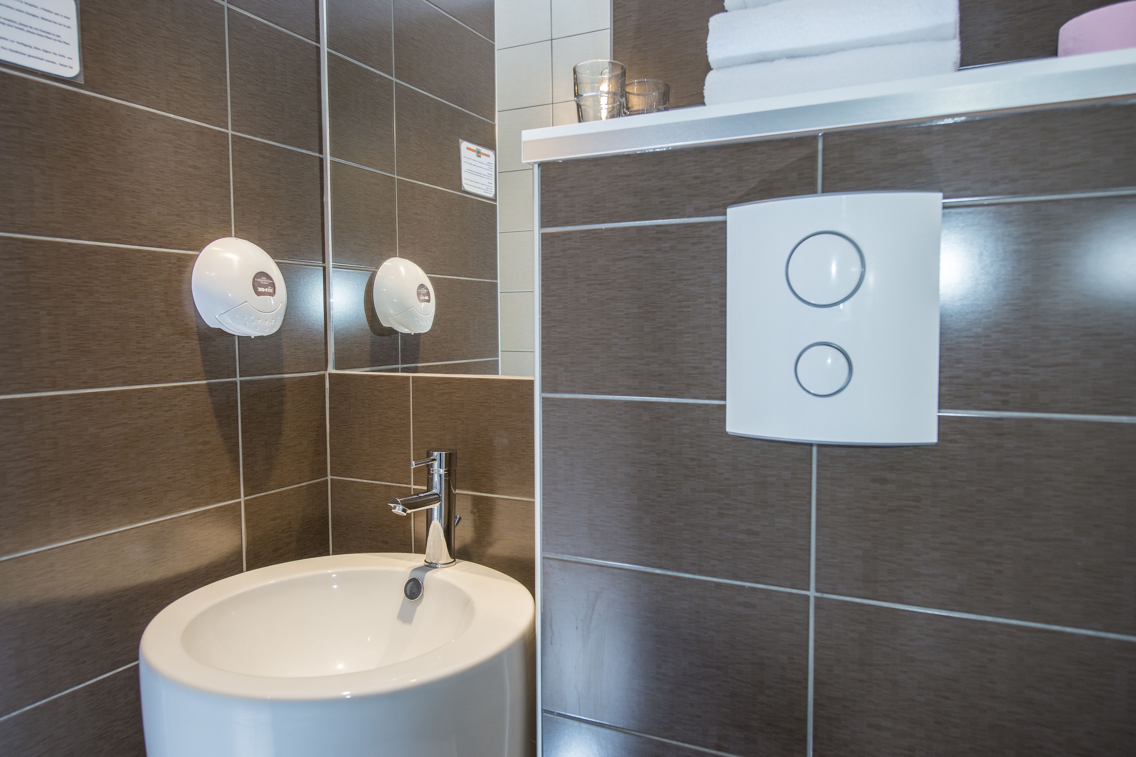 A modern bathroom with a white sink, two soap dispensers, and a towel rack.